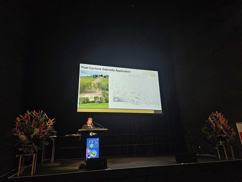 A person presenting at a podium with a projector screen
